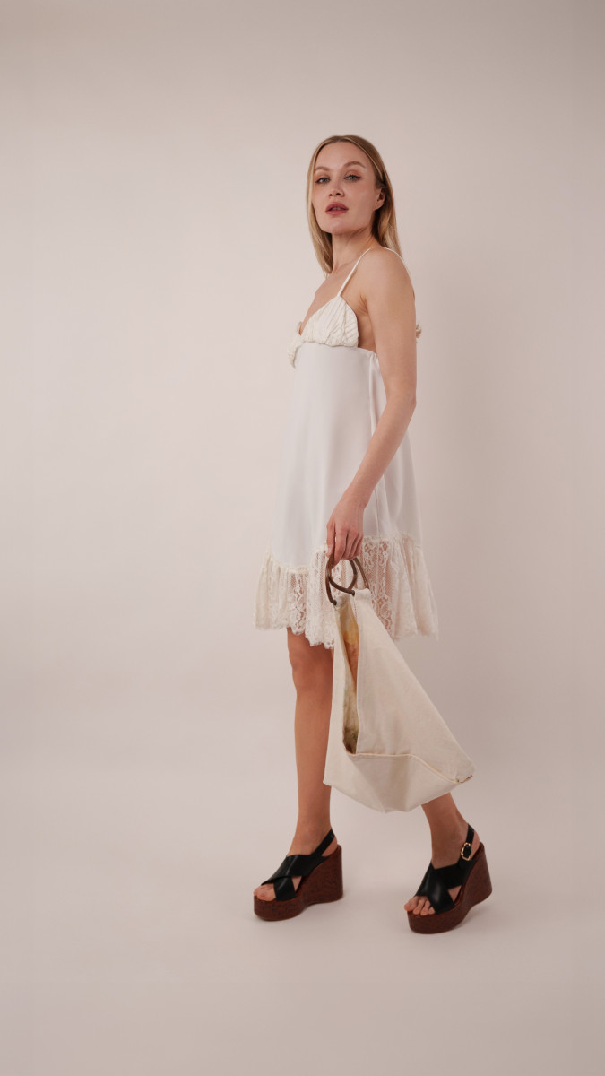 Model in the off-white lace Coral Bell Slip Dress holding an ivory Spirea Tote Bag for a final resort lunch in our vacation capsule.