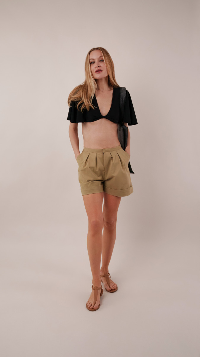 Model wearing a black Reed Swimsuit tucked into khaki Dresden Shorts, styled with a charcoal Spirea Tote Bag for a vacation capsule beach-to-lunch look.