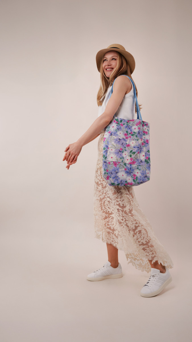 Model in a white Sylvan Tank Top and high-low lace Taiga Trapeze Skirt paired with white sneakers and a floral Spirea Tote Bag for a vacation capsule dinner look.