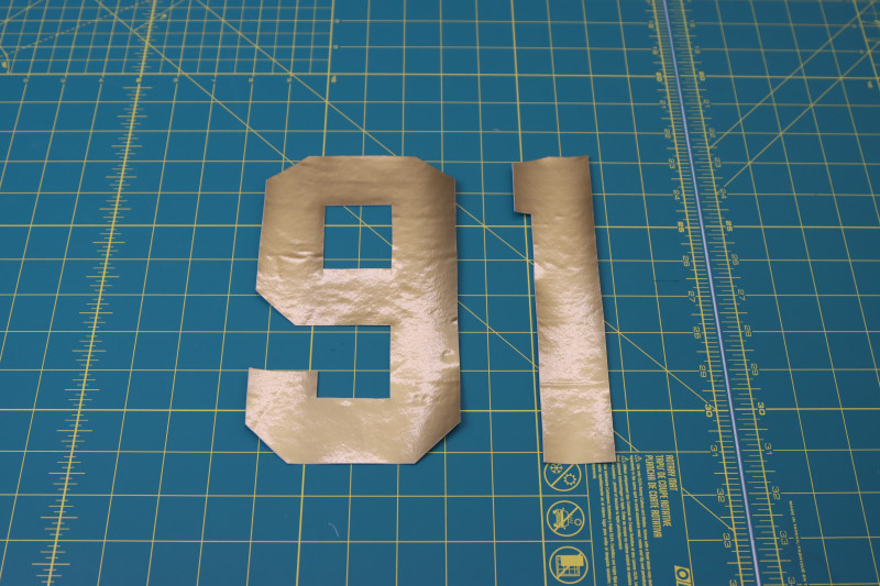 How To Cut Numbers Around Stencil - Gold Stretch Immitation Latex - Mood Fabrics - Fiona Athletic Set Free Sewing Pattern Tutorial - MDF537 - Mood Fabrics Sewciety Blog - Cut out the numbers around the stencil with a rotary cutter.