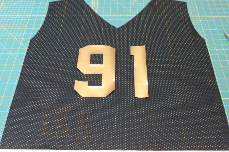 How To Place Numbers Front Jersey - Gold Stretch Immitation Latex - Mood Fabrics - Fiona Athletic Set Free Sewing Pattern Tutorial - MDF537 - Mood Fabrics Sewciety Blog - Place the numbers on the front of the jersey with the paper backing peeled off.